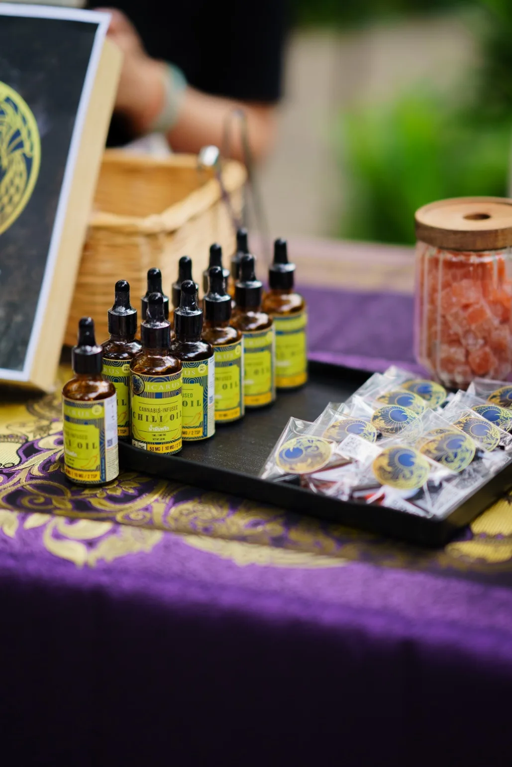 Bottles and packaged cannabis products are displayed on a purple tablecloth.