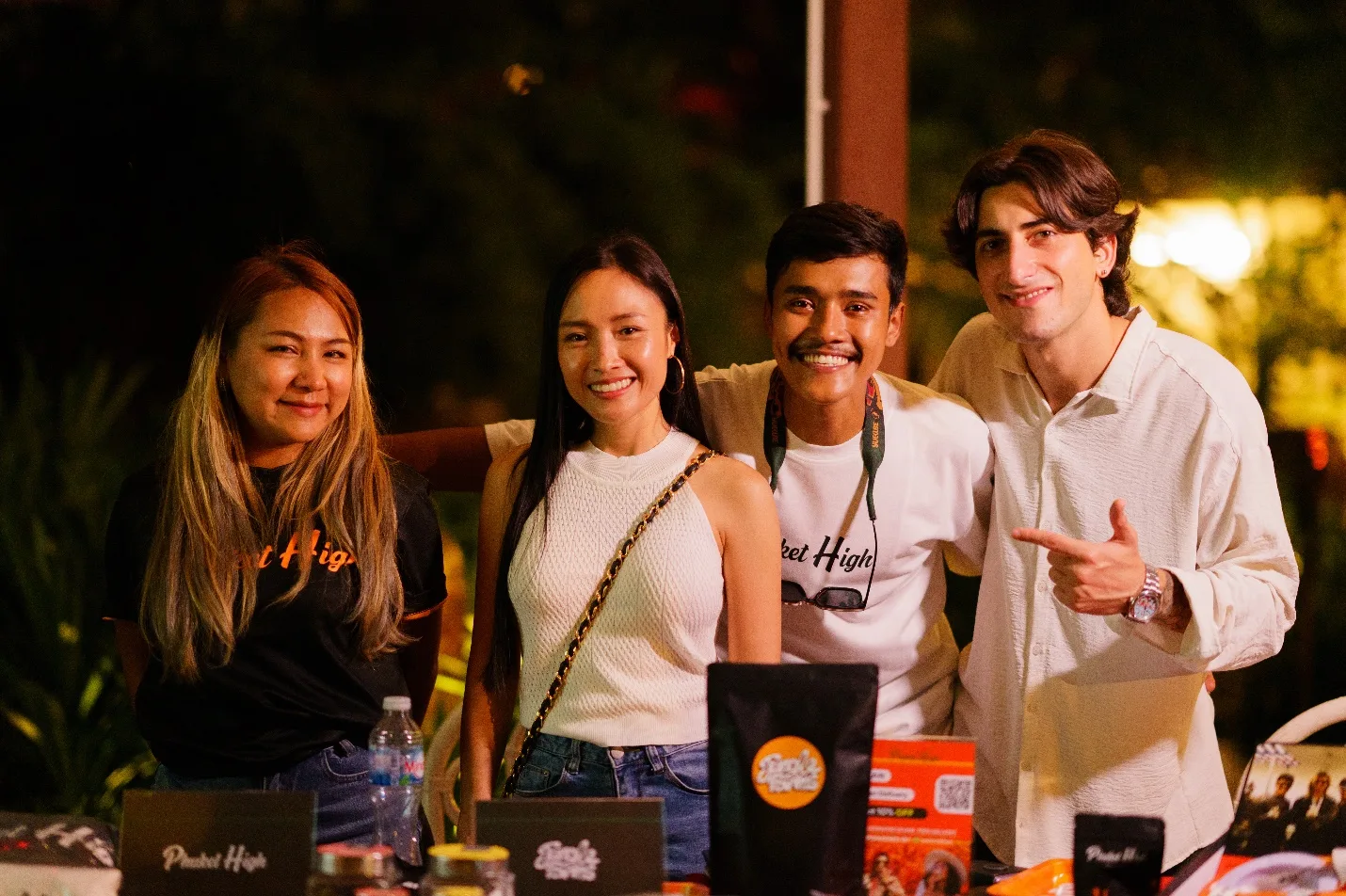 Four attendees pose together behind the Phuket High booth at night.